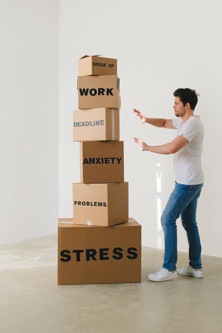 Mand med kasser stablet i et tårn på gulvet med forskellige ord på som "Stress, Problems, Anxiety, Deadline, Work, Break up"