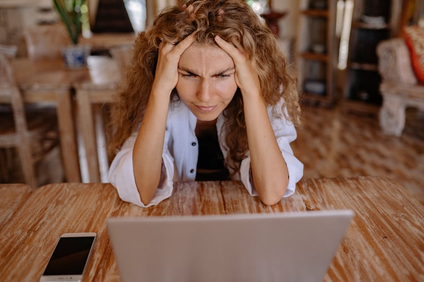Kvinde sidder ved bord med bærbar computer og tager sig til hovedet og ser opgivende ud